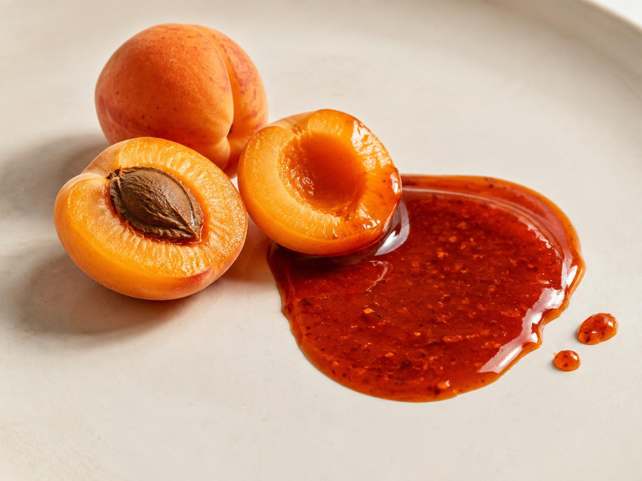 Chabacanos frescos junto a una salsa de chamoy brillante sobre cerámica crema